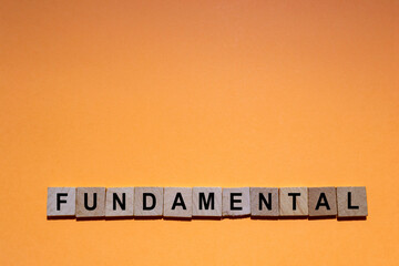 FUNDAMENTAL. Word written on square wooden tiles with an orange background. Horizontal photography.