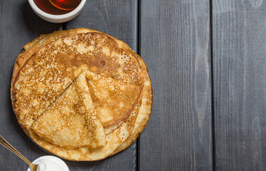 Pancakes with honey and sour cream on a dark wooden background, selective focus. Top view food, flat layout, copy space.