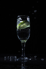 Piece of fresh cucumber splashing infused water in wineglass on black background in dark studio showing detox drink concept 