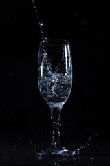 Fresh water splashing and pouring in crystal clear wineglass on black background on table in studio 