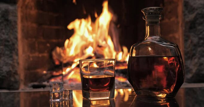 Bottle and glass with whiskey or cognac on the background of fire in the fireplace