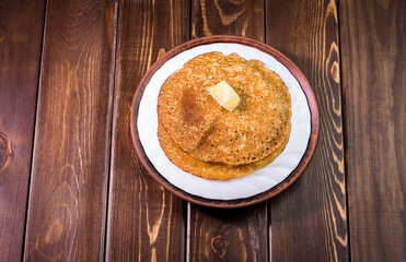 Russian pancakes with butter on a white dish and a dark wooden background close-up, isolate