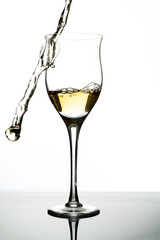 Serving a glass with white wine and pouring some of the liquid out of the glass. White background and backlighting. Concept of movement, elegance, taste.