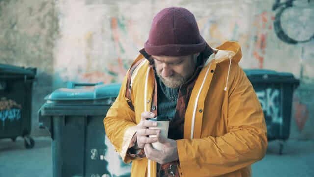 A beggar is drinking coffee next to the waste bins