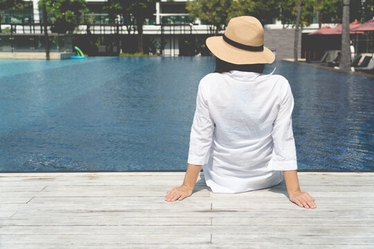 Woman with a straw hat sitting relaxing at the poolside. Girl at travel spa resort pool. Summer vacation.