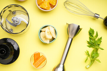 Hand blender and accessories with sliced fruit on a yellow background, closeup. Top view.