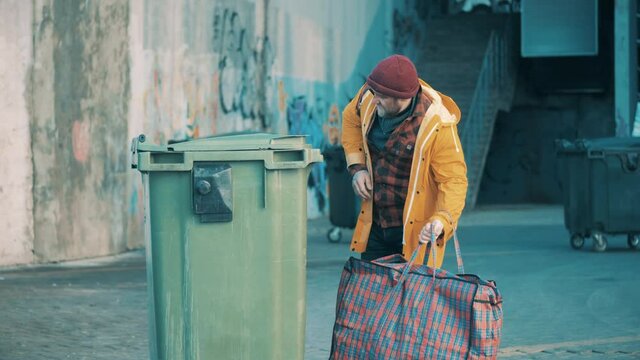A beggar is looking into a waste bin