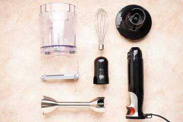 Black plastic electrical hand blender with stainless steel body and accessory on the beige background.