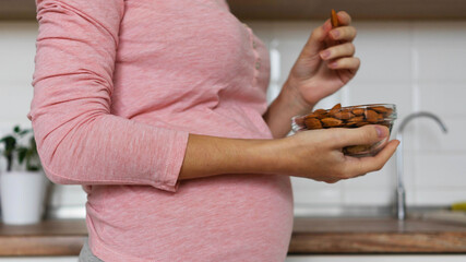 pregnant woman holding a bowl of nuts in her hand on the background of the home interior. Concept...