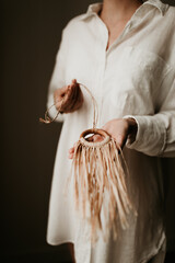 A woman is holding a brown wooden ring combined with raffia straw necklace in her hands. She is wearing white linen blouse. Soft natural light, on sustainable jewellery. Copy space. 