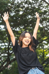 A young and carefree woman in a loose black shirt enjoying life, arms raised in joy. Looking at the...
