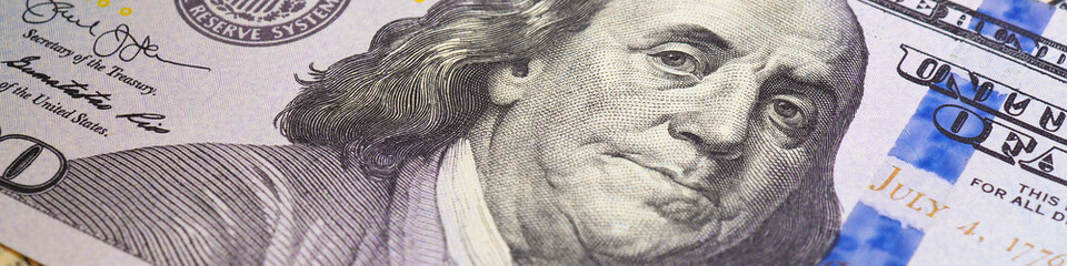 Obraz premium American paper money. A $100 bill with focus on eyes of Benjamin Franklin. US banknotes close-up. Savings economy and the USA dollar. Banner or headline. Macro