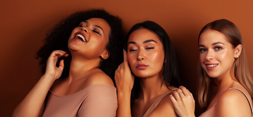 young pretty asian, caucasian, african woman posing cheerful together on brown background, lifestyle diverse nationality people concept