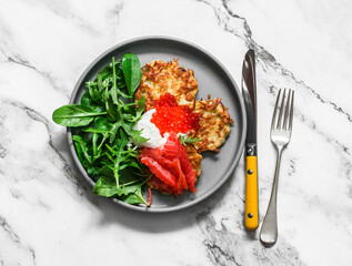 Potato latkes with red caviar, salty salmon, greek yogurt and green salad mix on a light background, top view