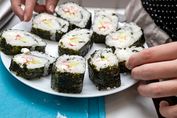 On a white plate, a girl smoothes homemade sushi.