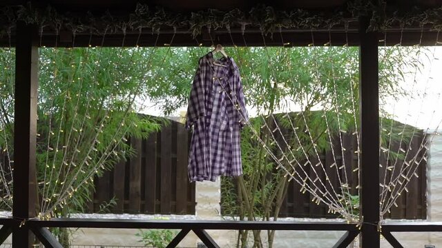A white and violet plaid shirt hangs on a hanger outside. Wet clothes dry in the wind and sun after washing. Clean male cloth after laundry at countryside outdoors.