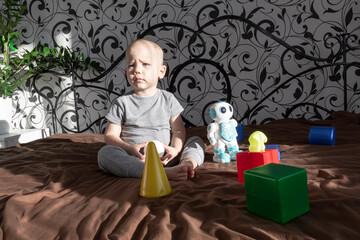 Naklejka premium A little boy is playing with a robot and various plastic toys, building a constructor on a bed in the interior of a room.