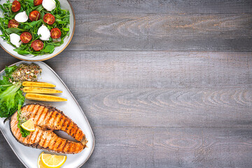Top table view of grilled salmon steak, mini corn, microgreen, salad and lemon on wooden table with copy space. Fried salmon steak and fresh salad and vegetables
