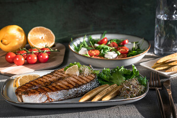 Grilled salmon steak, mini corn, microgreen, salad and lemon on wooden table. Fried salmon steak and fresh salad and vegetables