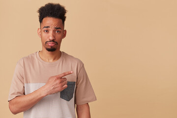 Studio portrait of young african american male points aside at copy space with sad, unhappy facial...
