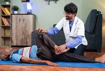 Physician exercising old man to stretch legs at home - concept of senior people home health check,...