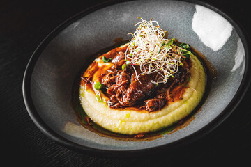 Stewed veal cheeks with mashed potatoes on plate on wooden table dark background