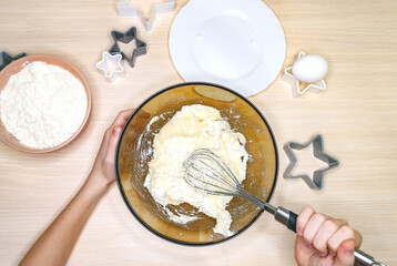 The child's hands mix the dough in a large bowl. The process of baking cookies at home. Flat lay.