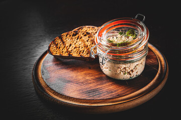 Jar of mackerel rillettes with toast on rustic wooden table dark background