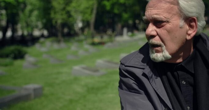 Sad old gray haired man sits on the grave at the cemetery, sorrow and sadness about lost of close people, 4k 60p Prores