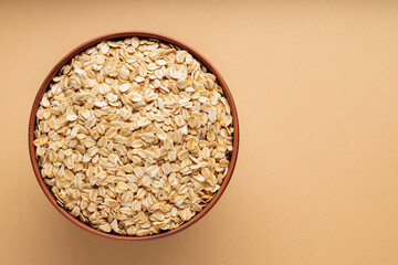 Oat flakes in a bowl. Dry rolled oatmeal on a beige background. Cooking oats porridge concept. Copy space. Top view