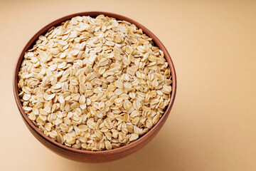 Oat flakes in a bowl. Dry rolled oatmeal on a beige background. Cooking oats porridge concept. Copy space. Top view