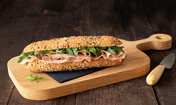 Ham sandwich with rocket leaves on wooden cutting board