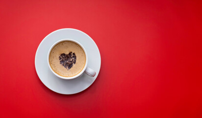 A mug of coffee with a chocolate heart on the foam stands on a monochromatic red background