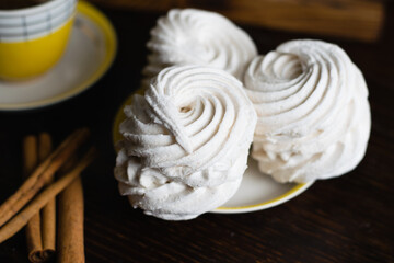 Aromatic marshmallow with cinnamon on a saucer and coffee in a vintage yellow cup on a dark background