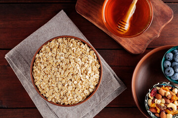 Oatmeal flakes, blueberries, honey and assorted nuts on a wooden background. Cereal and various delicious ingredients for breakfast. Top view