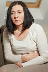 Fototapeta premium Middle aged mature woman suffering from stomach ache at home. Abdominal pain, food poisoning, diarrhea, stomach ulcer, menstruation pain, menopause.