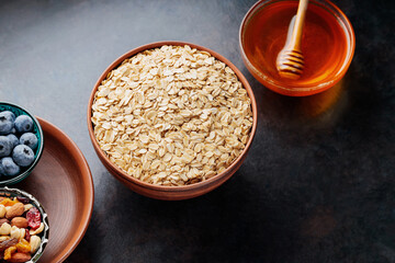 Oatmeal flakes, nuts, berries and honey on a dark background. Ingredients for healthy breakfast with oatmeal and blueberries. Top view