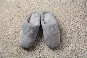 A female warm slippers on grey mat. Pair of comfortable slippers