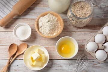 Frame of food ingredients for baking on a white background. Flour, eggs, sugar and milk in white and wooden bowls . Cooking and baking concept.