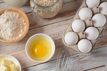 Frame of food ingredients for baking on a white background. Flour, eggs, sugar and milk in white and wooden bowls . Cooking and baking concept.