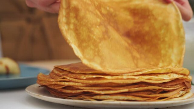 Anonymous cook taking a pancake from a plate with several pancakes on it