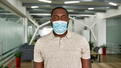 Black man in medical mask look at camera in office