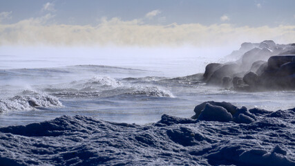 Waves crash against the icy Lake Michigan shoreline with steam coming off the water in subzero temperatures. Taken at Gillson Beach in Wilmette, Illinois.