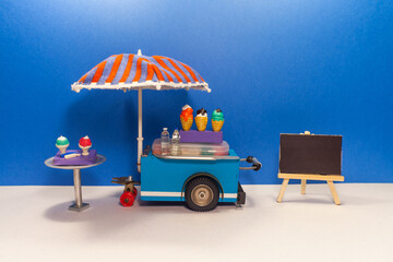 Mini shop Ice cream cart with blue red umbrella. Assortment of ice cream empty menu black chalkboard. blue wall background - 479204181