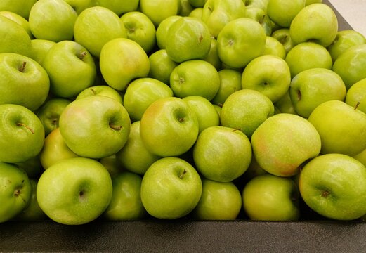 Ripe Granny Smith apples loosely scattered in a traditional vegetable market display, closeup image.