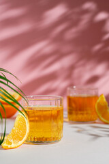two glasses with an orange cocktail on the table on a sunny day. Pink background. Orange slices