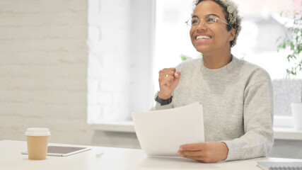 African Woman Celebrating Success while Reading Documents in Office