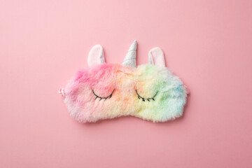 Top view photo of funny multicolored fluffy unicorn sleeping mask on isolated pastel pink background