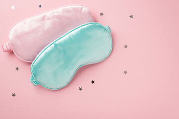Fototapeta premium Top view photo of two light pink and blue silk sleeping masks and star shaped confetti on isolated pastel pink background with empty space