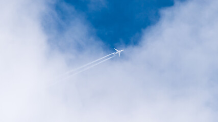 a passenger airliner flying out of white clouds against a blue sky background. Passenger airliner in the sky. Condensation or inversion trace of jet engines.